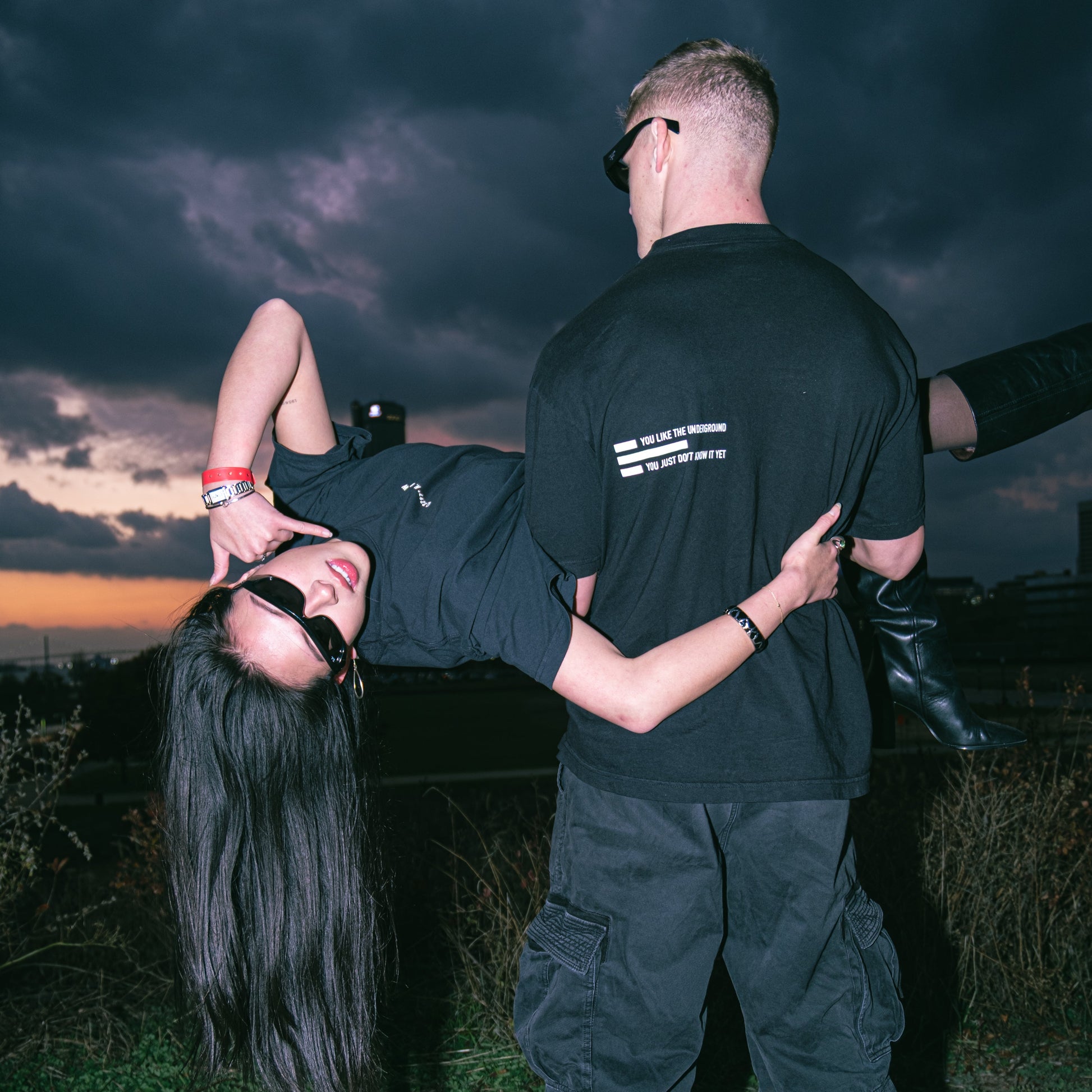 Two people in black outfits against a dark, stormy sky.